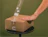 A hand smoothing transparent tape with white text 'YOU'RE WEIRD I LIKE THAT' onto a cardboard box on a stool