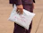 A person in a dark outfit holding a white poly mailer bag printed with red 'MONÉBARI MAROQUINERIE' branding