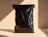 A plain black glossy poly mailer bag standing upright on a beige surface in bright sunlight