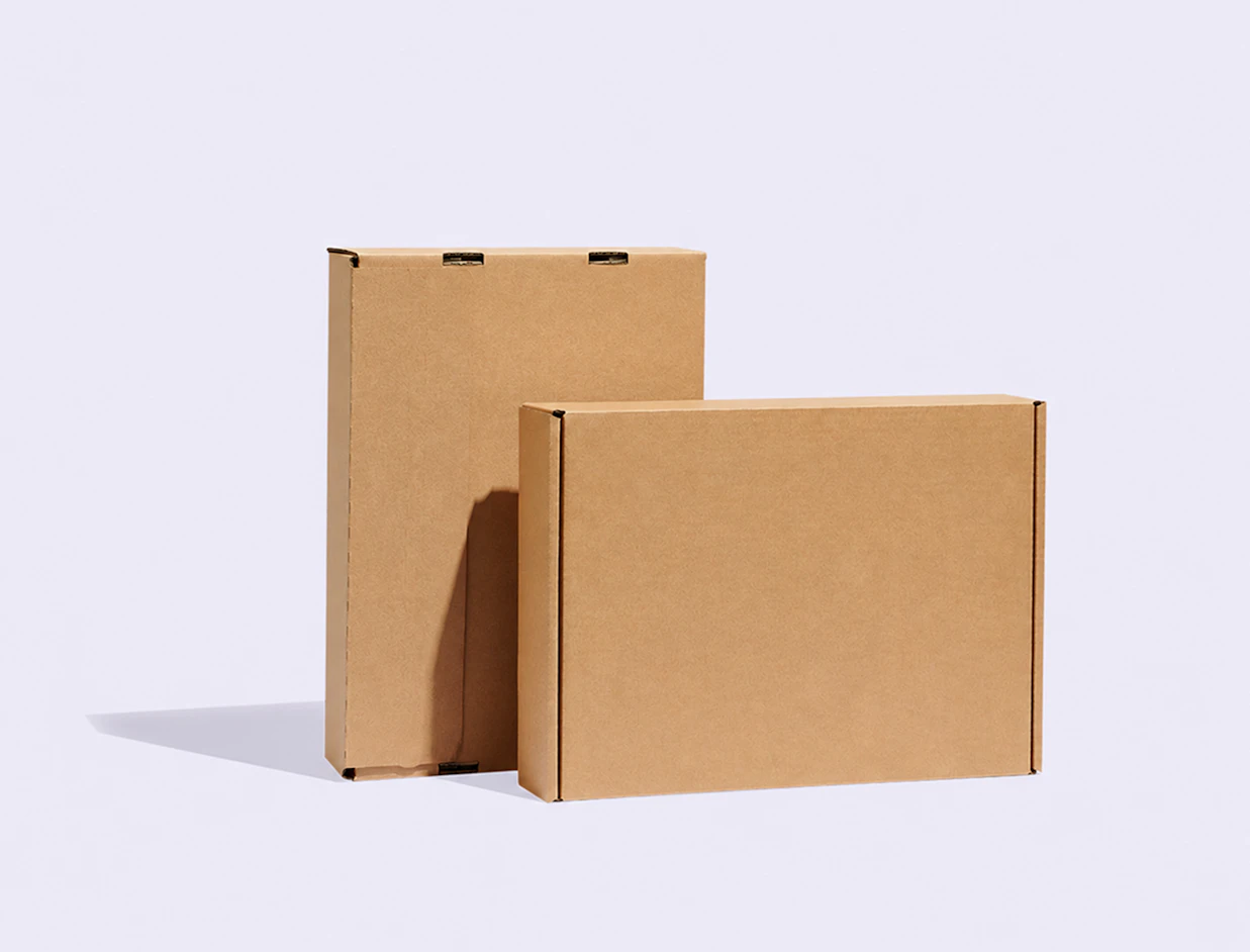 Two plain brown corrugated cardboard laptop boxes standing upright against a light grey background