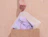 Hand placing a frosted zipper bag with a folded lilac T-shirt into a kraft paper bag