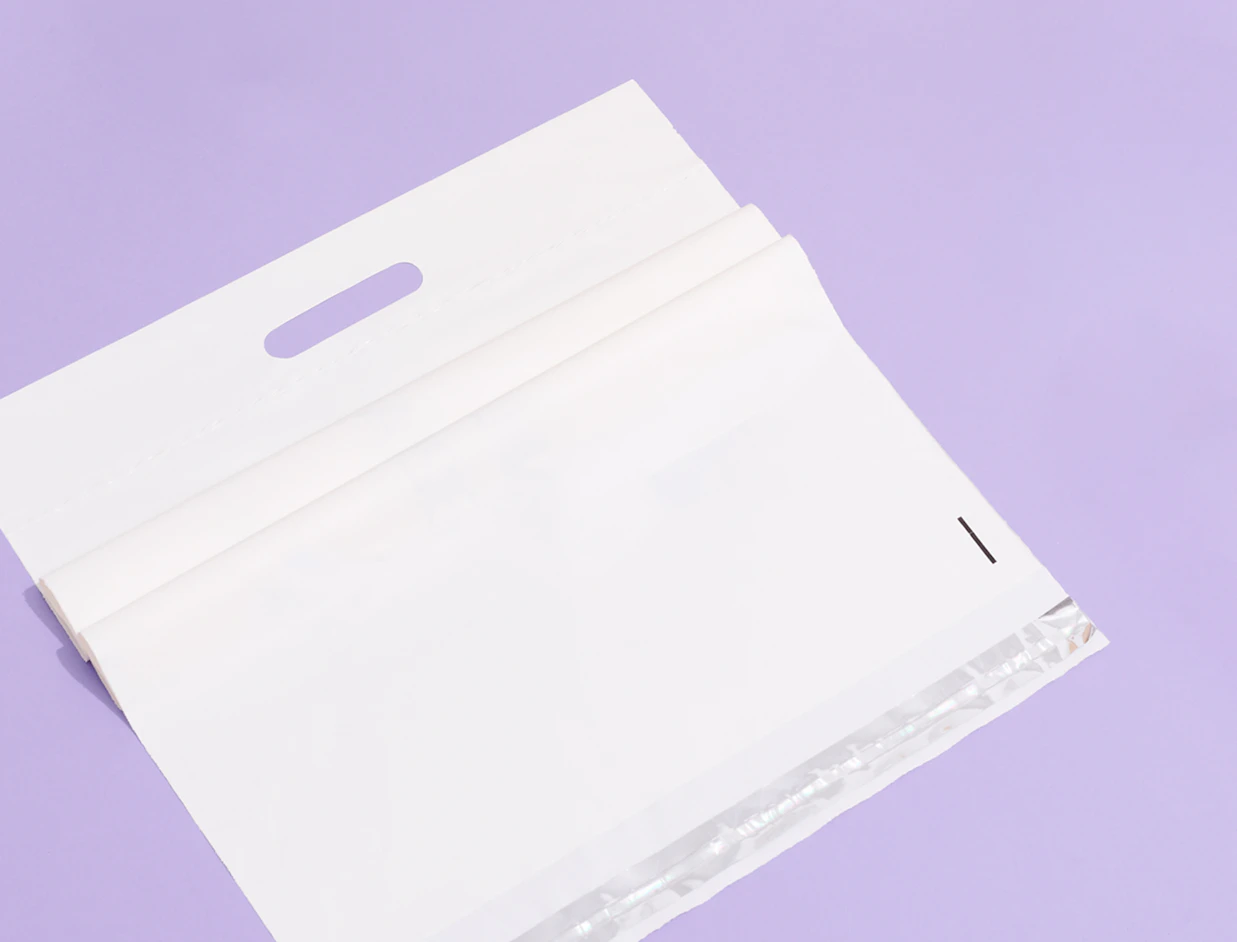 Close-up view of a folded white padded envelope with a die-cut handle and metallic silver interior lining on a light purple background