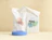 Two white biodegradable poly mailers printed with colorful abstract shapes and 'Hey, I'm fully biodegradable' text displayed on a blue cylindrical pedestal