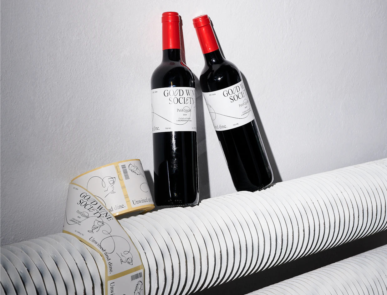 Two wine bottles with rectangular white custom labels next to a label roll