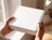 Hands holding a blank white corrugated cardboard mailer box near a window