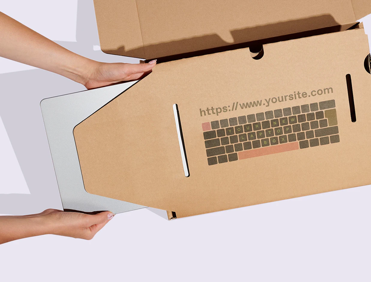 Hands sliding a silver laptop into a custom cardboard shipping insert printed with a keyboard illustration and website URL