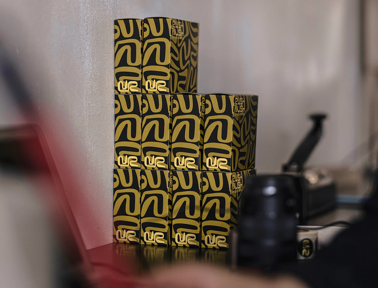 A vertical stack of black and yellow patterned coffee boxes labeled 'Rush Mush Coffee Roasters'