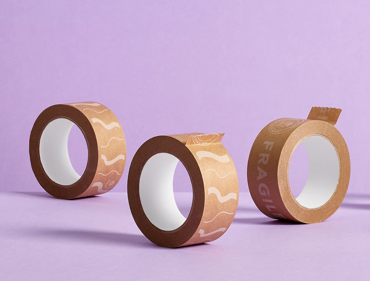 Three rolls of brown paper packaging tape, two with printed wavy lines and one printed with 'FRAGILE', standing upright on a purple background