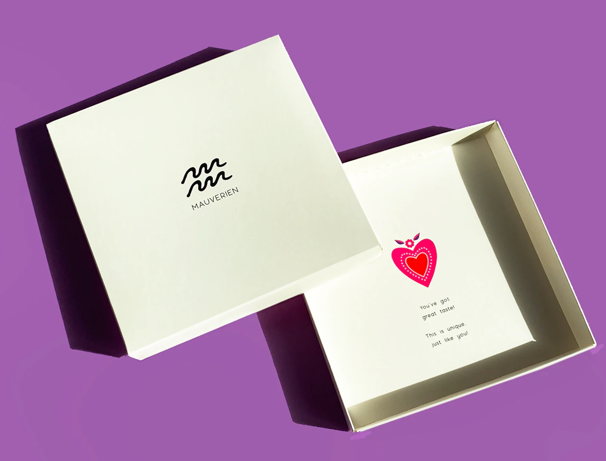 An open white gift box branded 'MAUVERIEN' revealing a printed heart illustration and message inside, set against a purple background
