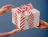 Hands handing over a white gift box wrapped with a red and white diagonal striped ribbon bow on a blue backdrop