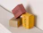 Three printed product boxes in pink, beige and yellow with bold lettering