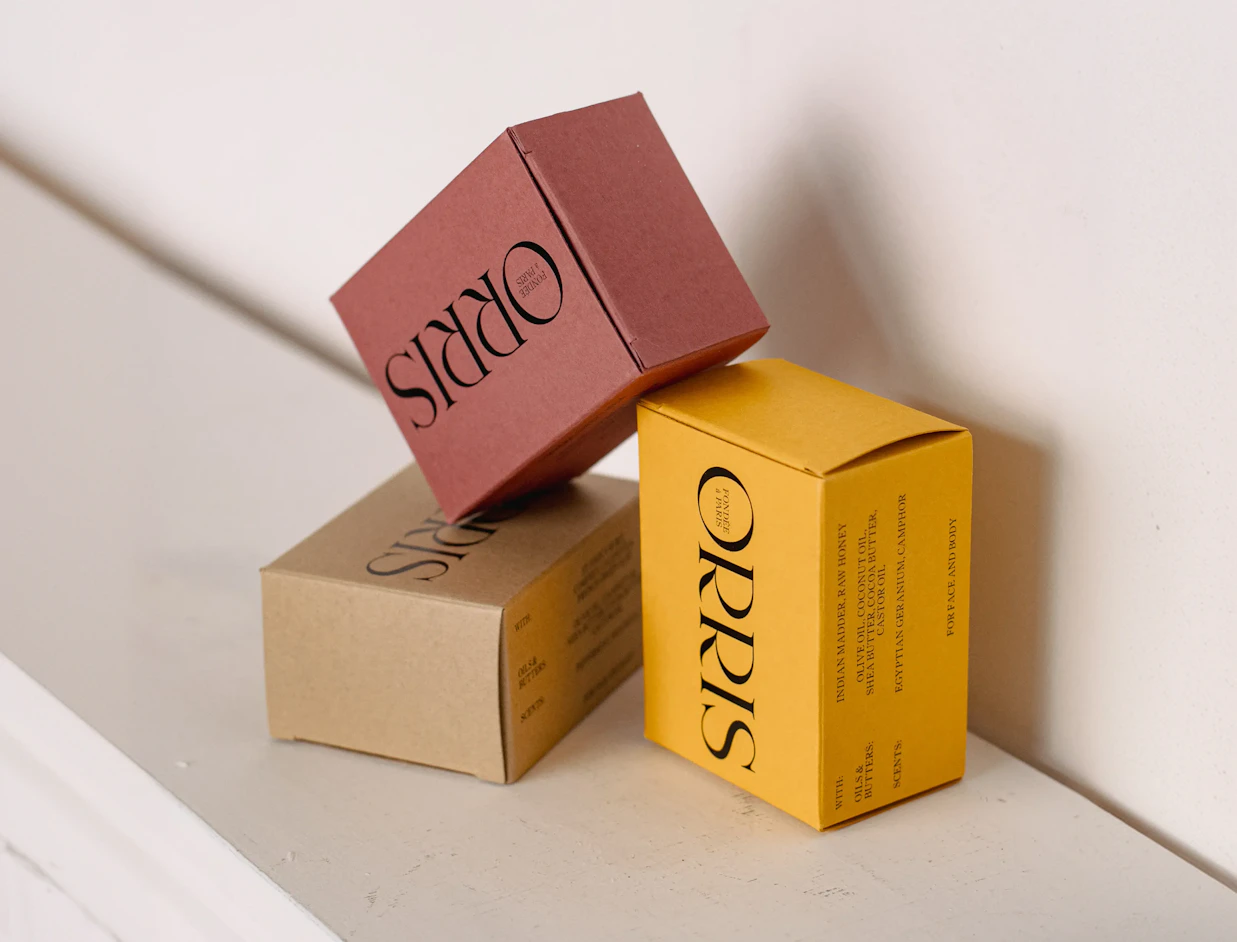 Three printed product boxes in pink, beige and yellow with bold lettering