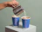 A hand pouring milk from a metal pitcher into a blue paper cup labeled 'ROAST' filled with iced coffee